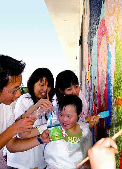  义 工 与 患 有 唐 氏 综 合 症 的 女 童 在 玛 嘉 烈 戴 麟 趾 红 十 字 会 学 校 携 手 绘 画 壁 画 。 