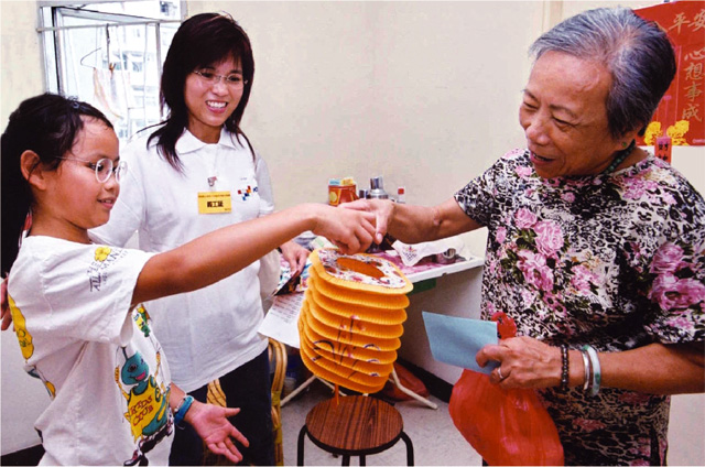 A young primary school volunteer presents a lantern to an elderly woman during the Mid-Autumn Festival.